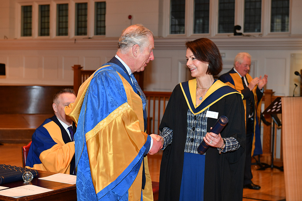 A man and a woman both in robes, shaking hands and smiling